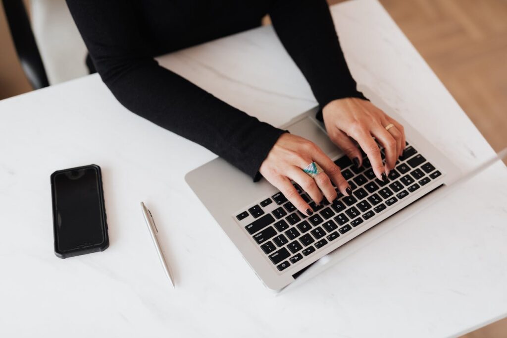 From above of crop anonymous young female programmer typing on netbook keyboard while sitting at table with smartphone in modern workspace